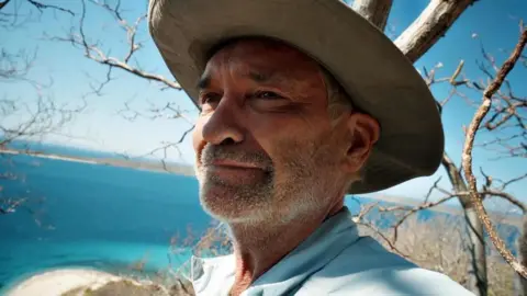 Channel 5 Phillip Schofield smiling in front of the beach and the sea